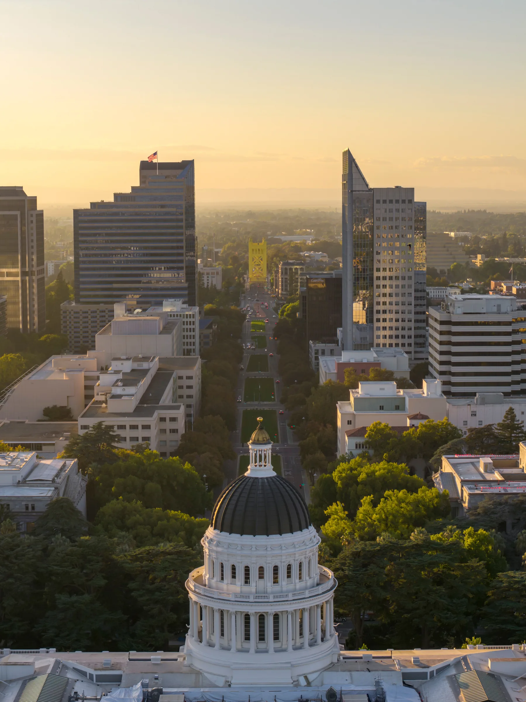 Aerial view of California state capitol building dome with downtown Sacramento skyline at sunset.