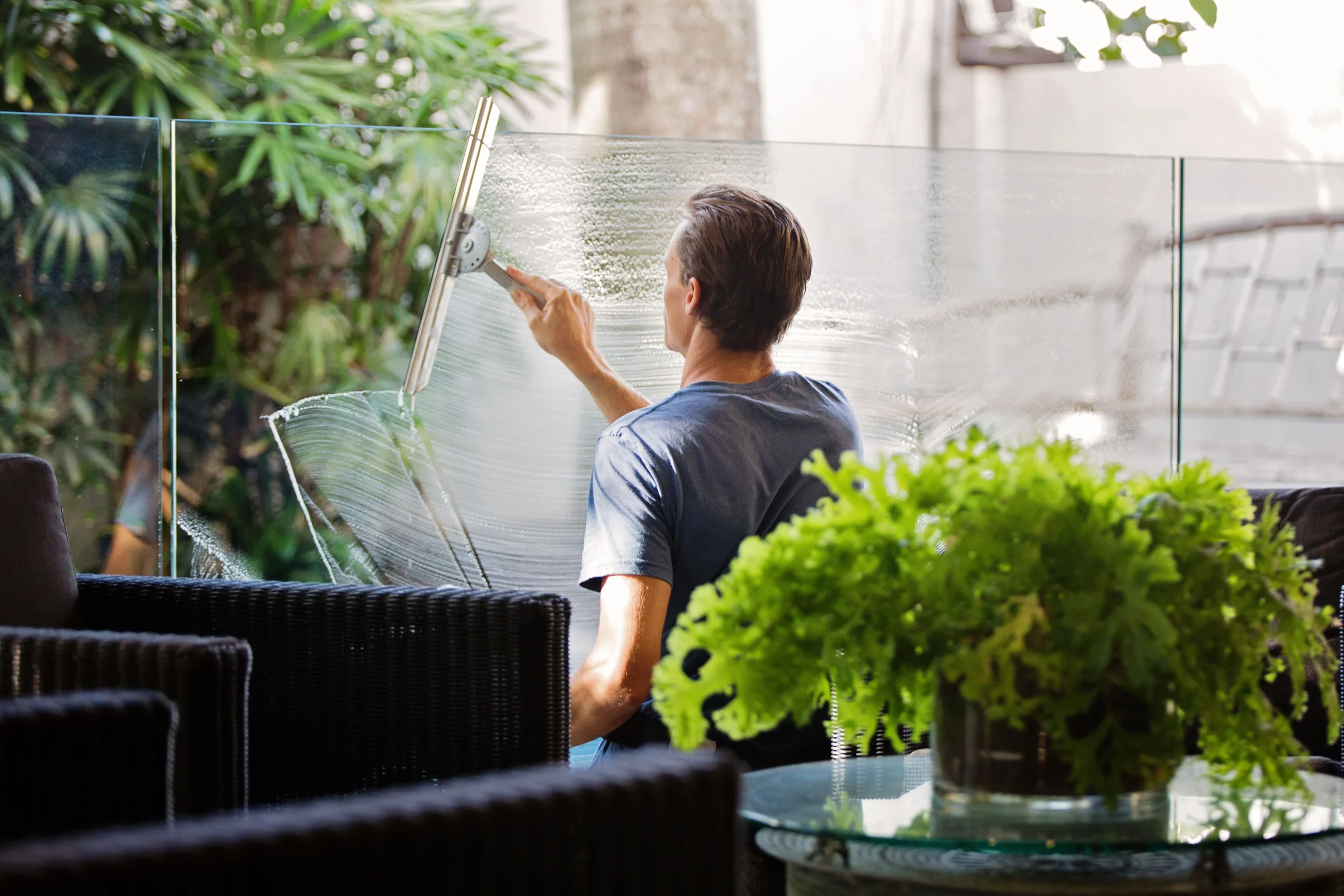 Man cleaning an exterior glass panel with a squeegee tool outdoors.