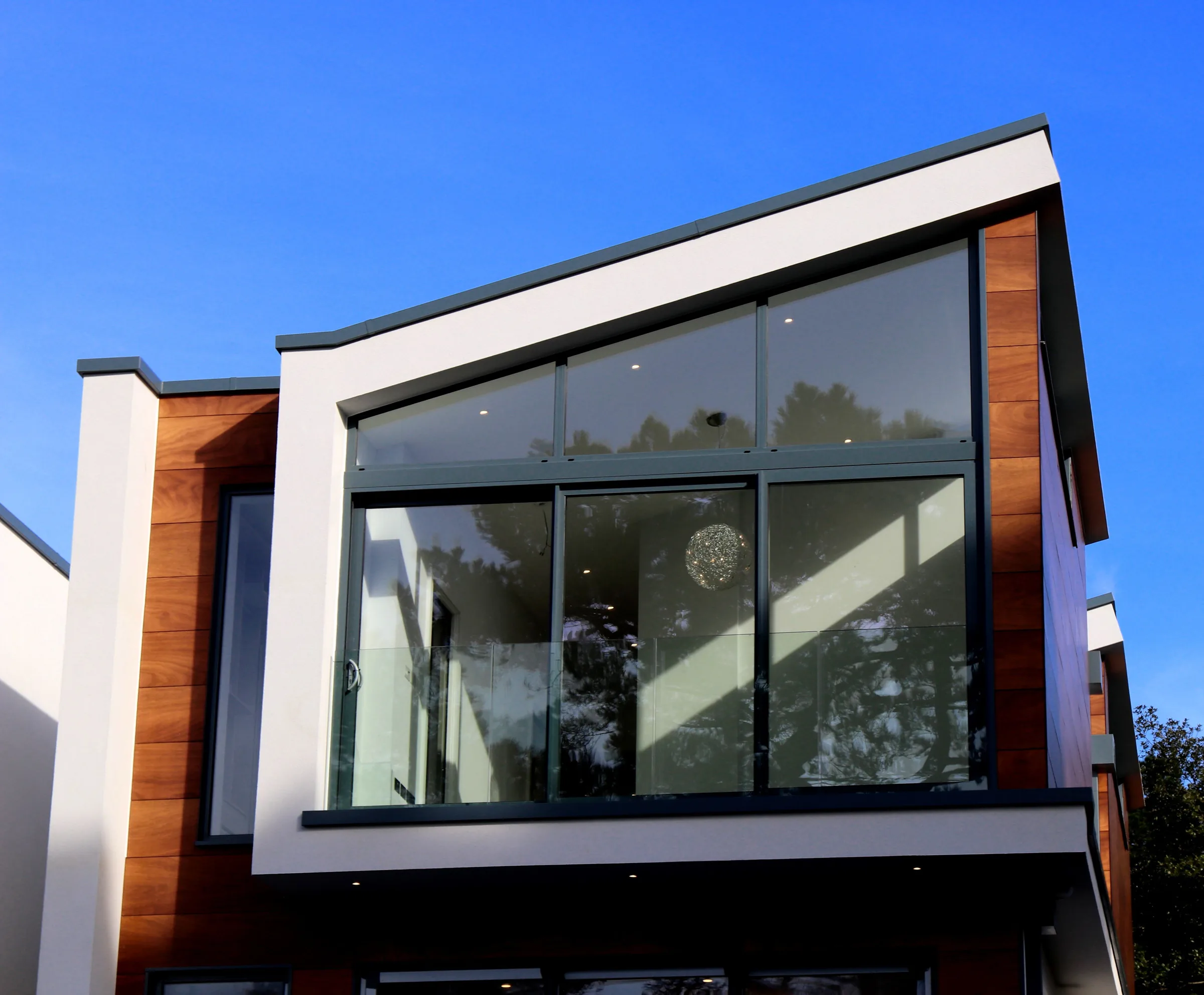 Modern home with large clean windows and white and wood exterior against blue sky.